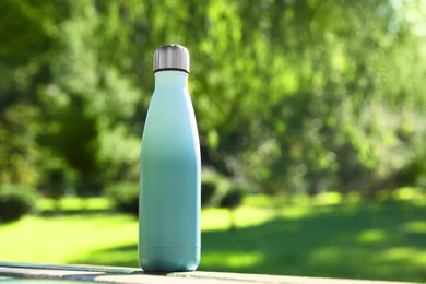 Photo of Thermo bottle on wooden bench in park, space for text