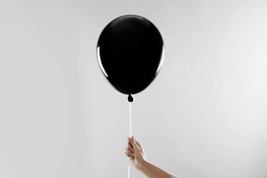 Woman holding black balloon for Halloween party on light grey background, closeup