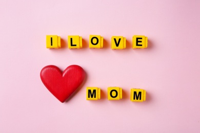 Photo of Phrase I LOVE MOM made of plastic letters and wooden heart on color background, top view