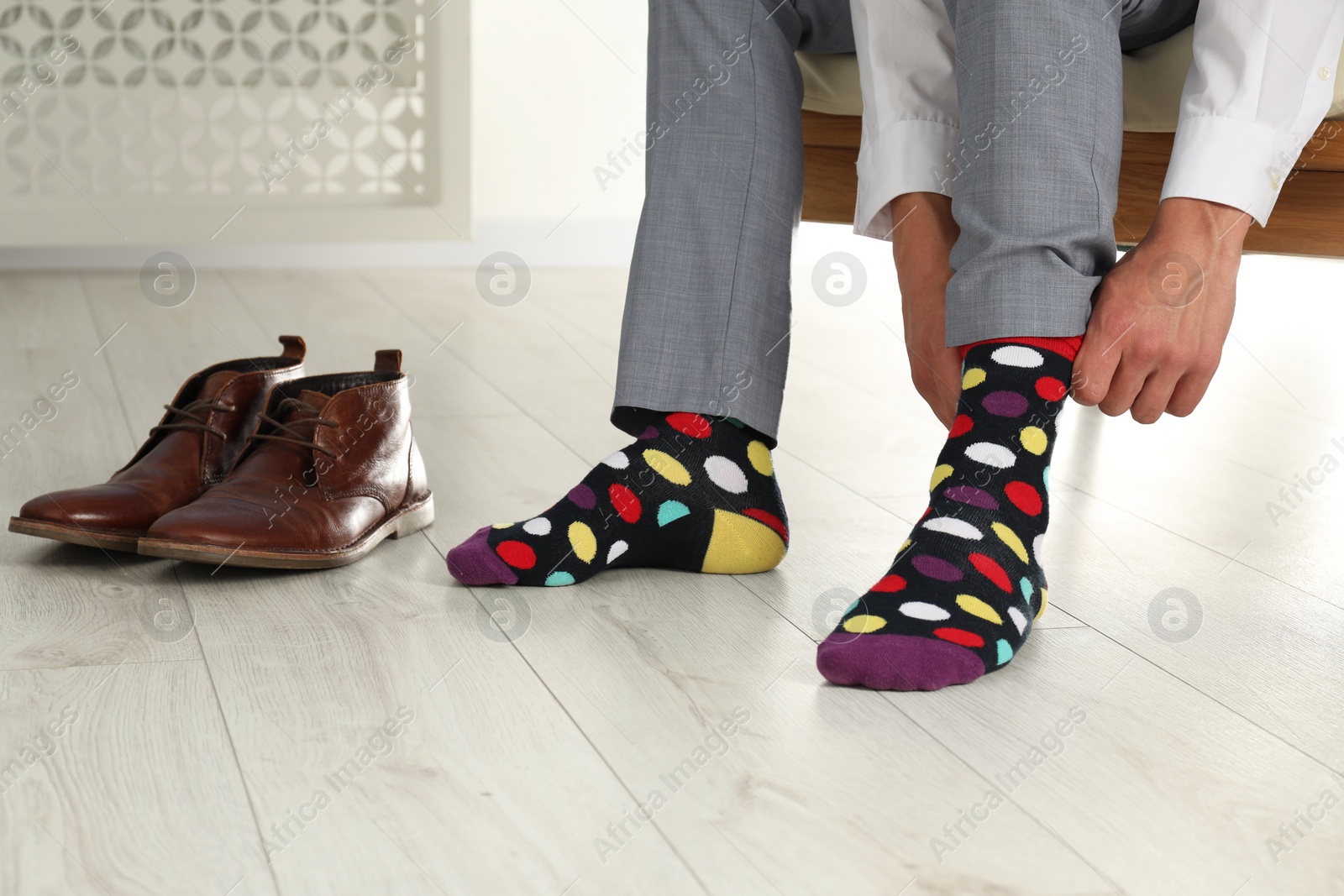 Photo of Man putting on colorful socks indoors, closeup