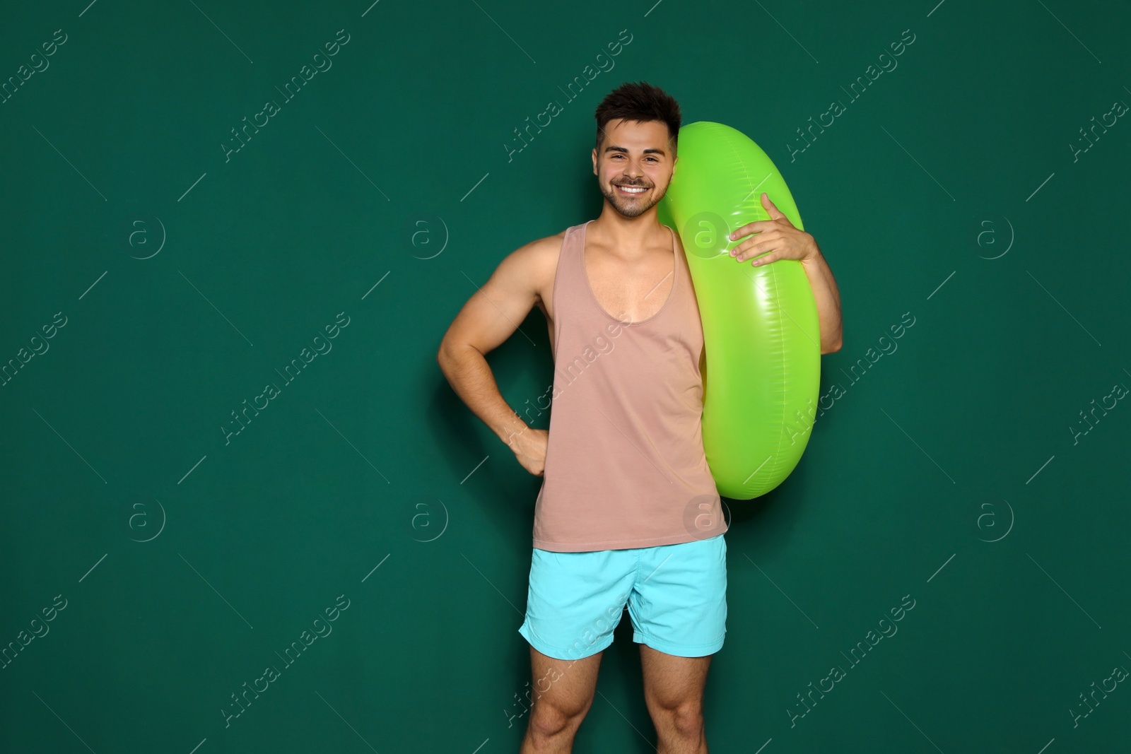 Photo of Funny young man with bright inflatable ring on dark green background, space for text