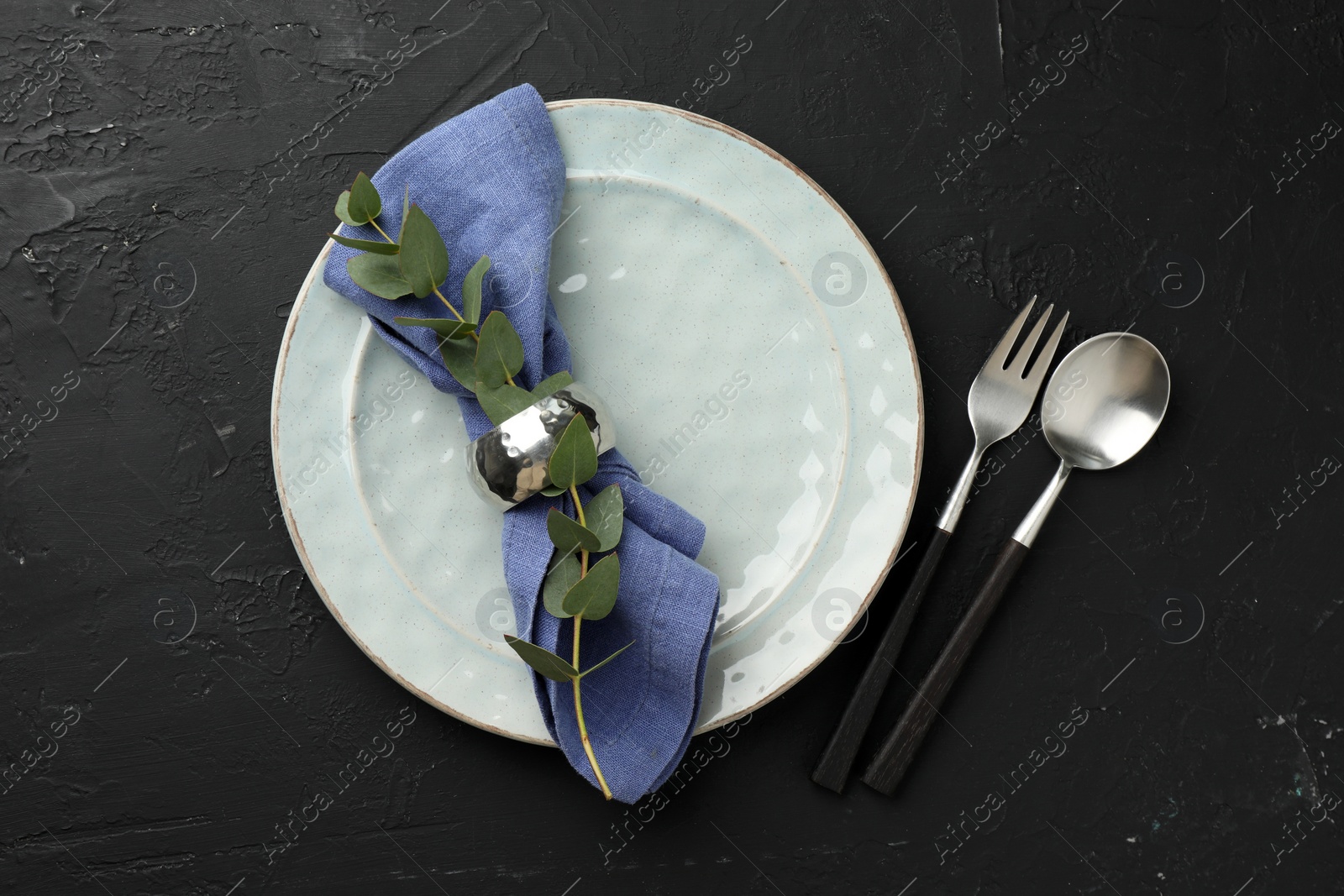 Photo of Stylish setting with cutlery, eucalyptus branch, napkin and plate on dark textured table, top view