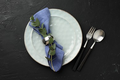 Stylish setting with cutlery, eucalyptus branch, napkin and plate on dark textured table, top view