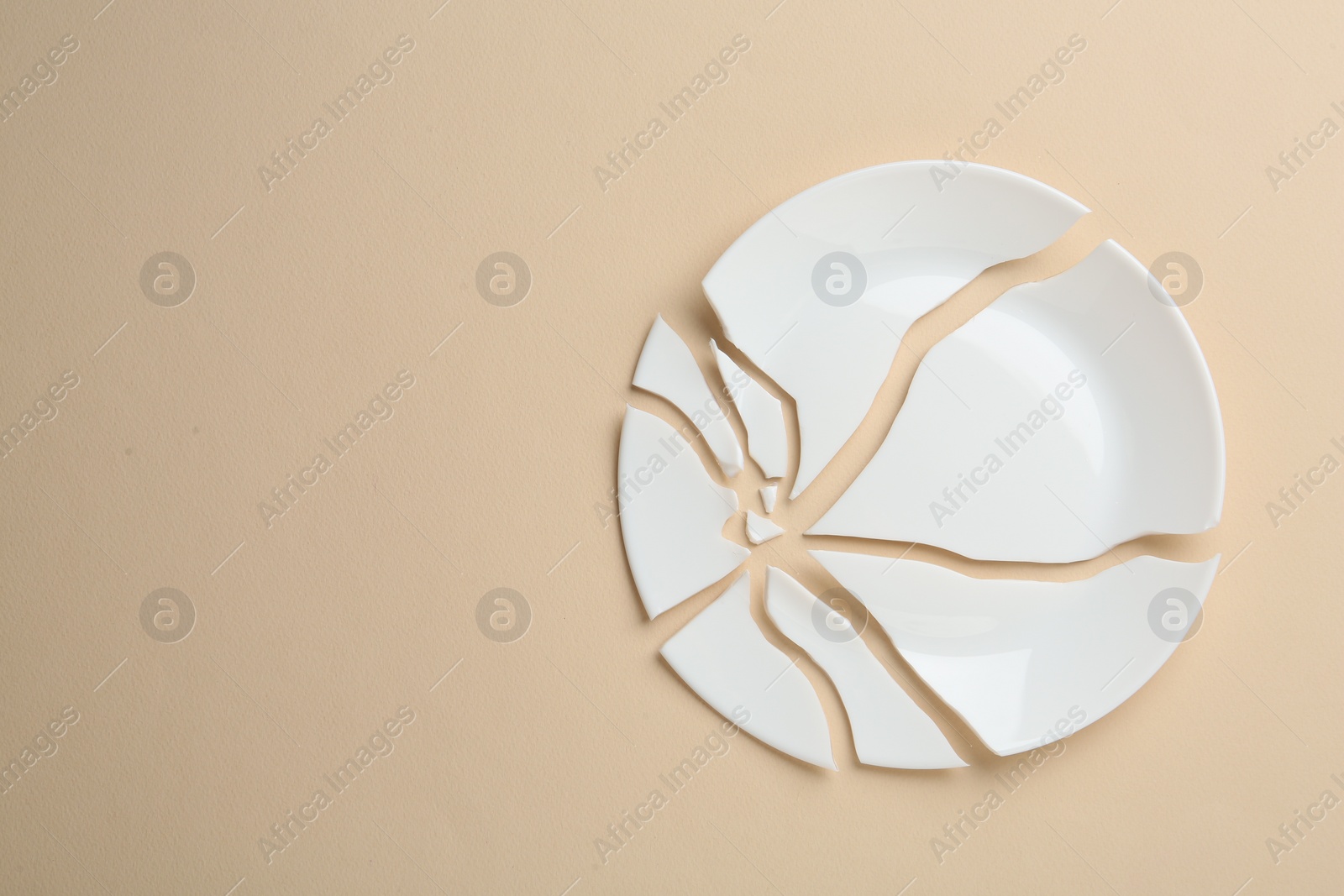 Photo of Pieces of broken ceramic plate on beige background, flat lay. Space for text