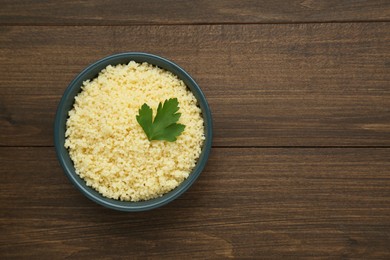 Photo of Tasty couscous with parsley on wooden table, top view. Space for text
