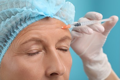 Photo of Doctor giving facial injection to senior woman on light blue background, closeup. Cosmetic surgery