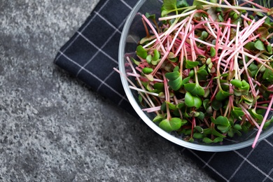 Glass bowl with fresh microgreen on grey table, flat lay. Space for text