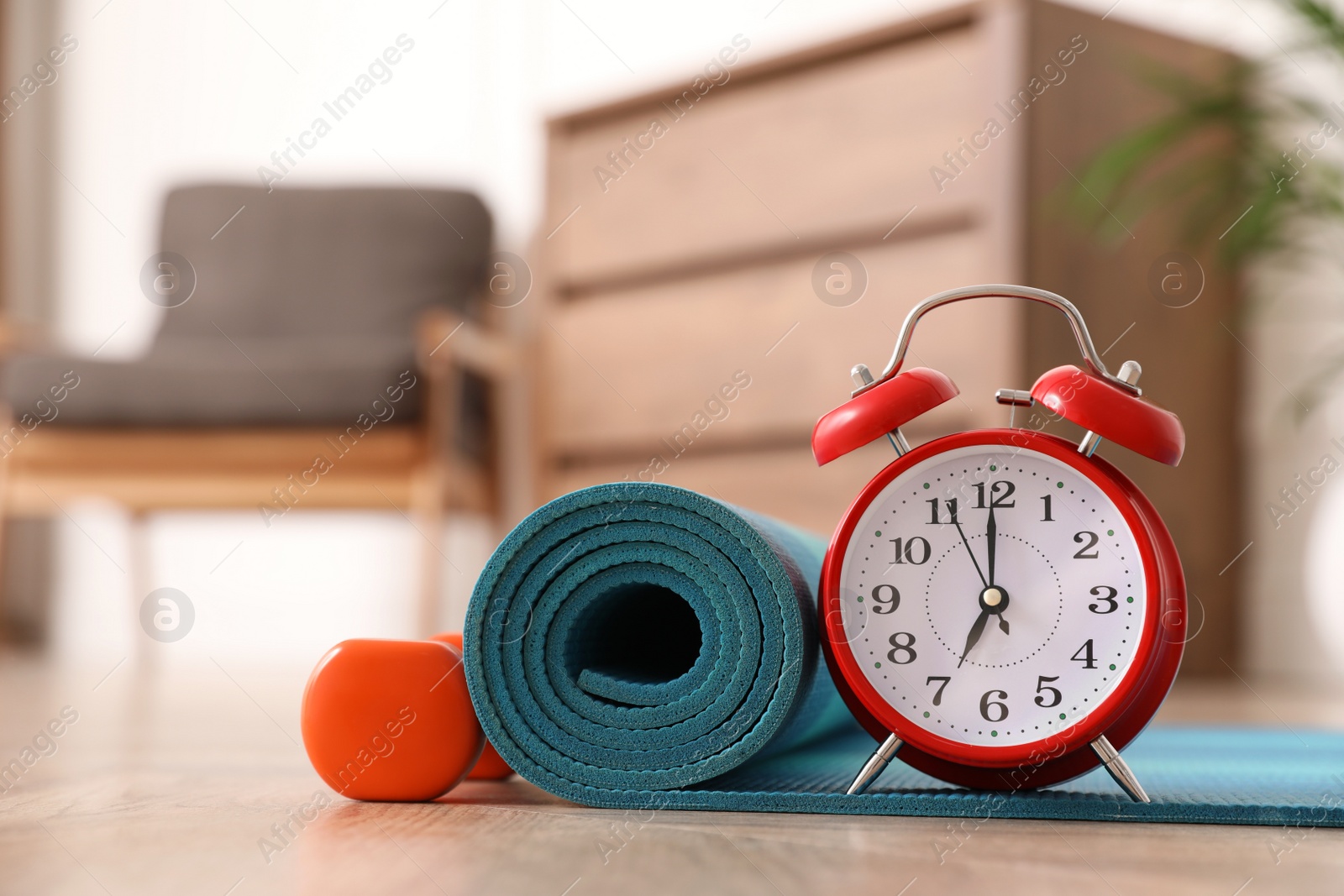 Photo of Alarm clock, yoga mat and dumbbells on wooden floor indoors. Morning exercise