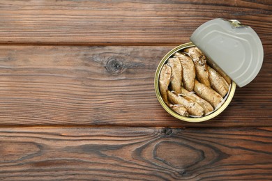 Open tin can of sprats on wooden table, top view. Space for text