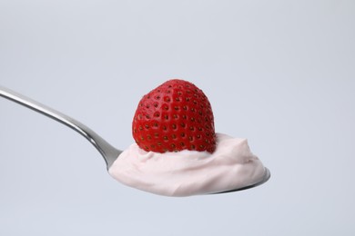 Photo of Delicious natural yogurt with fresh strawberry in spoon on light background