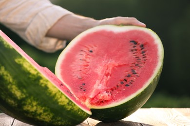 Man with tasty ripe watermelon at wooden table outdoors, closeup