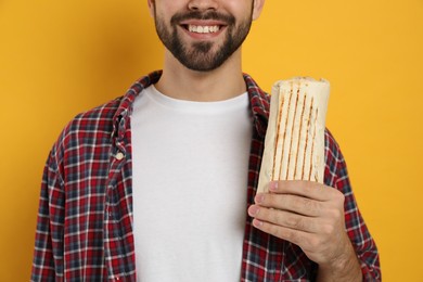 Happy young man holding tasty shawarma on yellow background, closeup