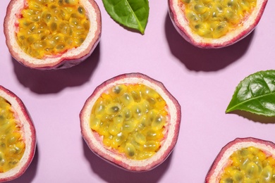 Photo of Halves of passion fruits (maracuyas) and green leaves on pink background, flat lay