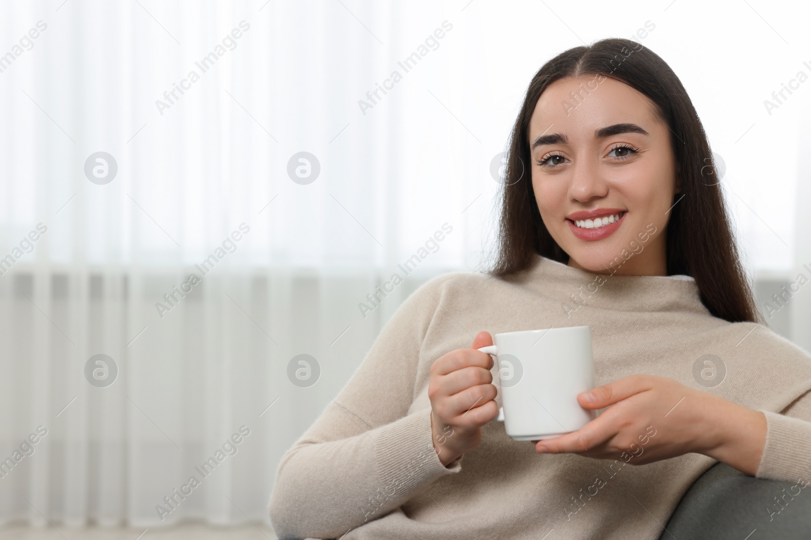 Photo of Happy young woman holding white ceramic mug at home, space for text