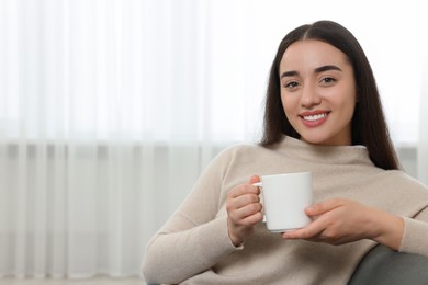 Photo of Happy young woman holding white ceramic mug at home, space for text