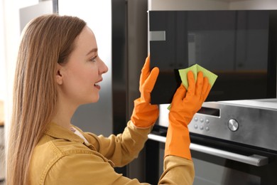 Photo of Woman with microfiber cloth cleaning microwave in kitchen