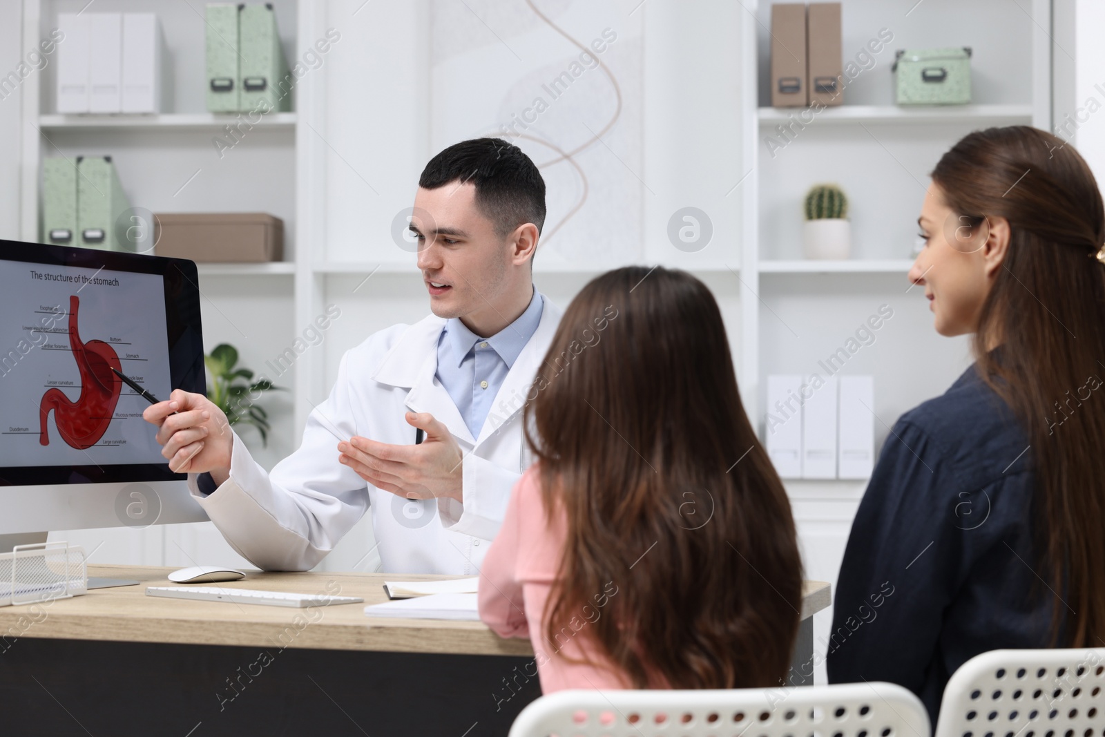 Photo of Gastroenterologist consulting woman with her daughter and showing image of stomach on computer in clinic