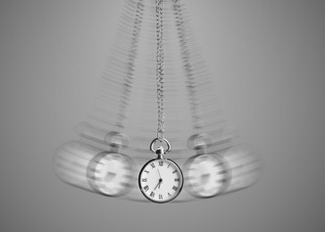 Image of Hypnosis session. Vintage pocket watch with chain swinging on grey background, motion effect