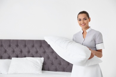 Photo of Young chambermaid with pillow in hotel room. Space for text
