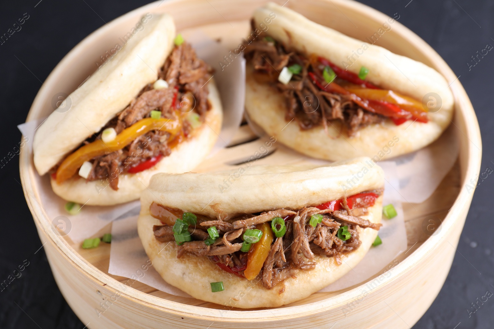 Photo of Delicious gua bao in bamboo steamer on black table, closeup