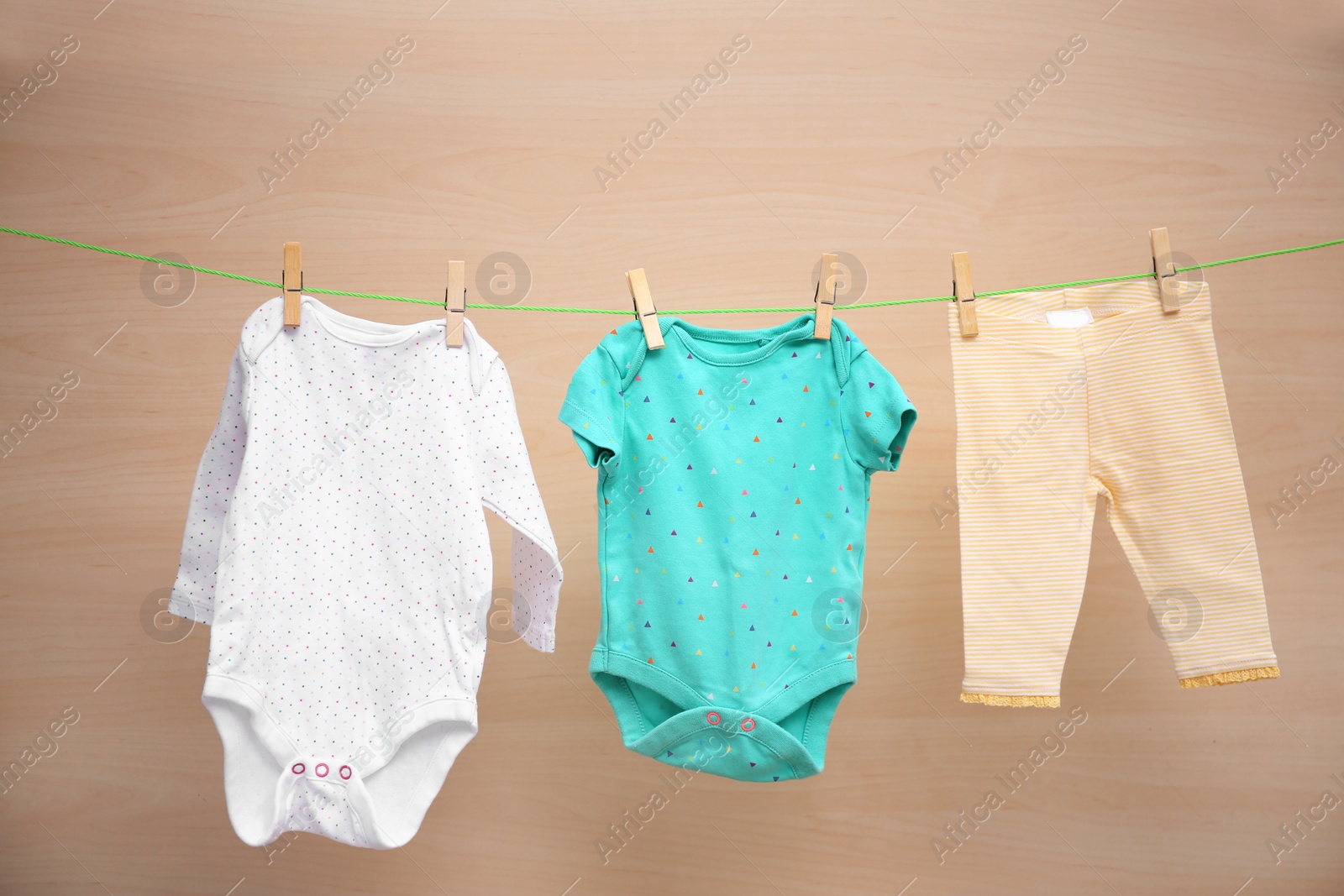 Photo of Baby clothes hanging on washing line against wooden background