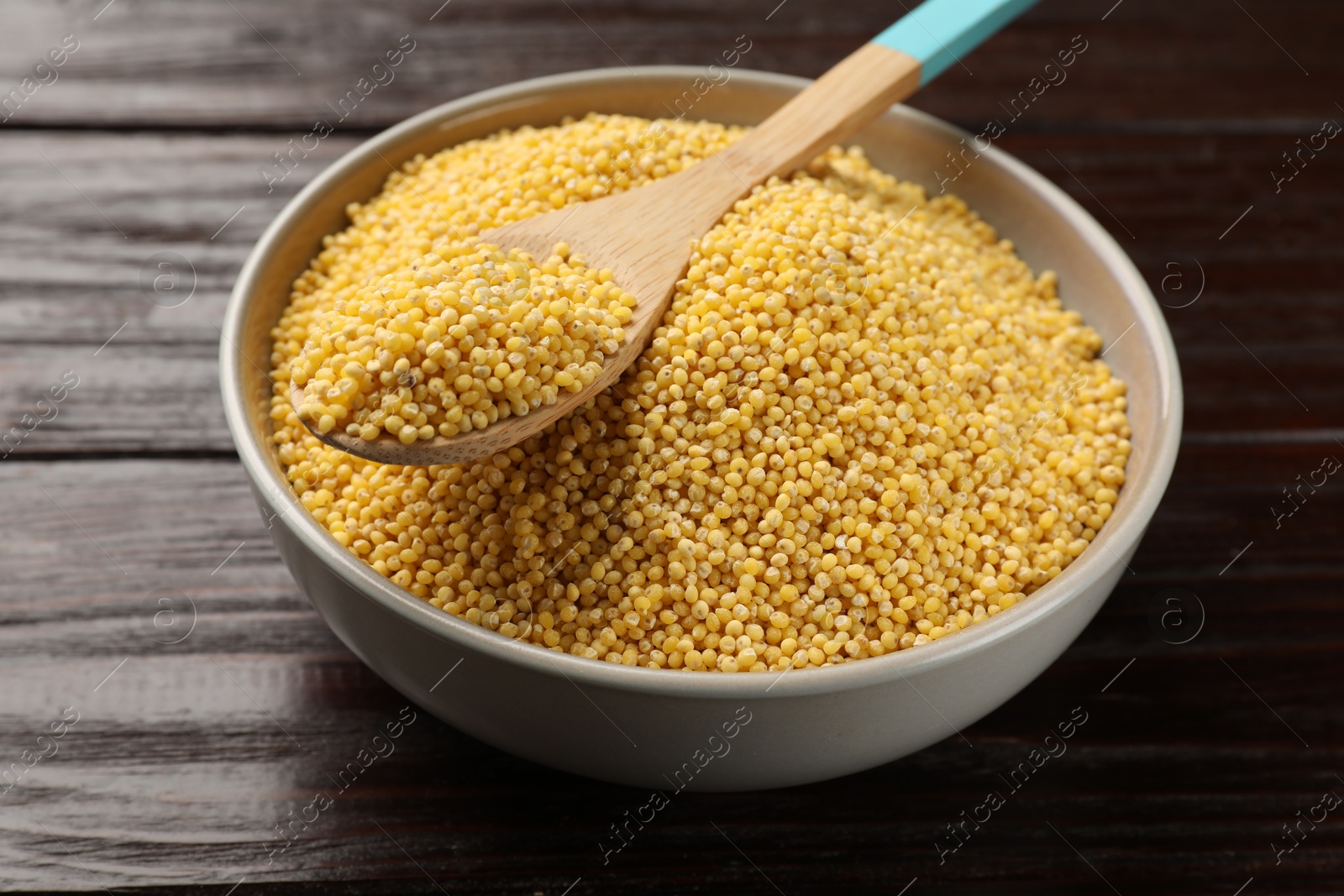 Photo of Millet groats in bowl and spoon on wooden table, closeup