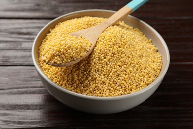 Photo of Millet groats in bowl and spoon on wooden table, closeup