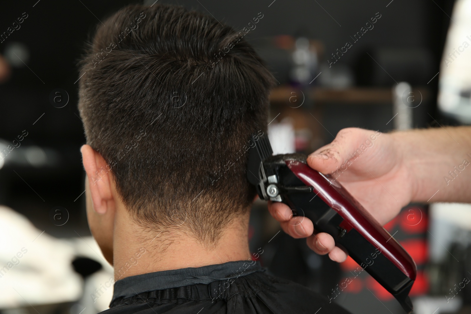 Photo of Professional barber making stylish haircut in salon, closeup