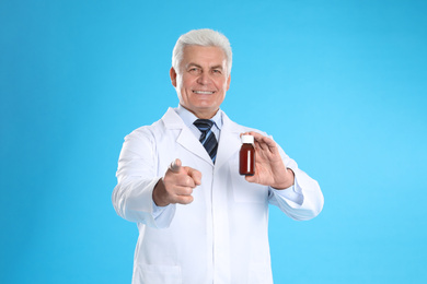 Photo of Senior pharmacist with syrup on light blue background