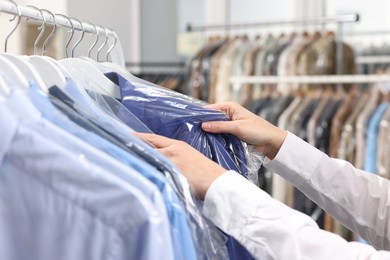 Photo of Dry-cleaning service. Woman taking shirt in plastic bag from rack indoors, closeup