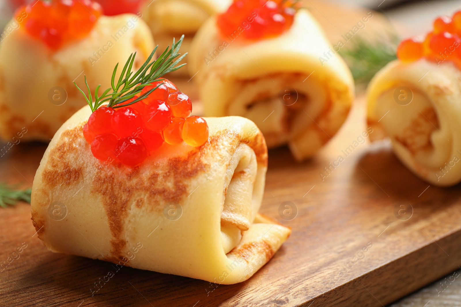 Photo of Delicious thin pancakes with red caviar on wooden board, closeup