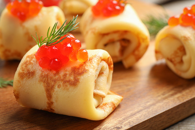 Delicious thin pancakes with red caviar on wooden board, closeup