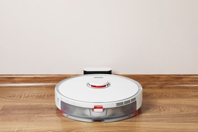 Robotic vacuum cleaner charging on wooden floor indoors