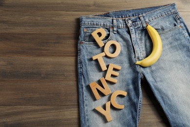 Photo of Men jeans with banana and word Potency made of letters on wooden table, top view. Space for text
