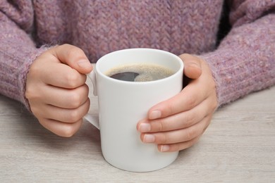 Photo of Woman holding white mug with coffee at wooden table, closeup