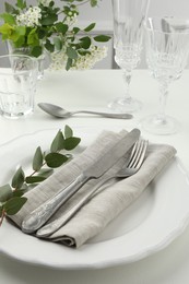 Stylish setting with cutlery, eucalyptus leaves and plate on white textured table, closeup