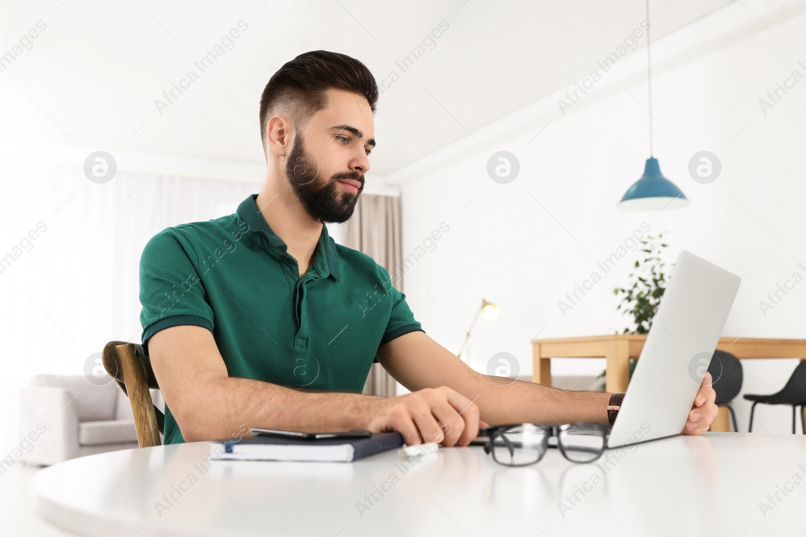 Photo of Handsome young man working with laptop at table in home office