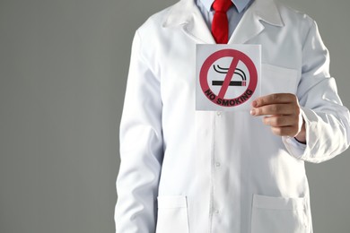 Doctor holding card with no smoking sign on gray background, closeup. Space for text