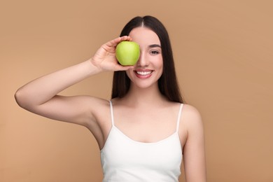 Beautiful young woman with apple on beige background