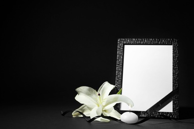 Photo of Funeral photo frame with ribbon, white lily and candle on black background. Space for design