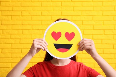 Woman covering face with heart eyes emoji near yellow brick wall