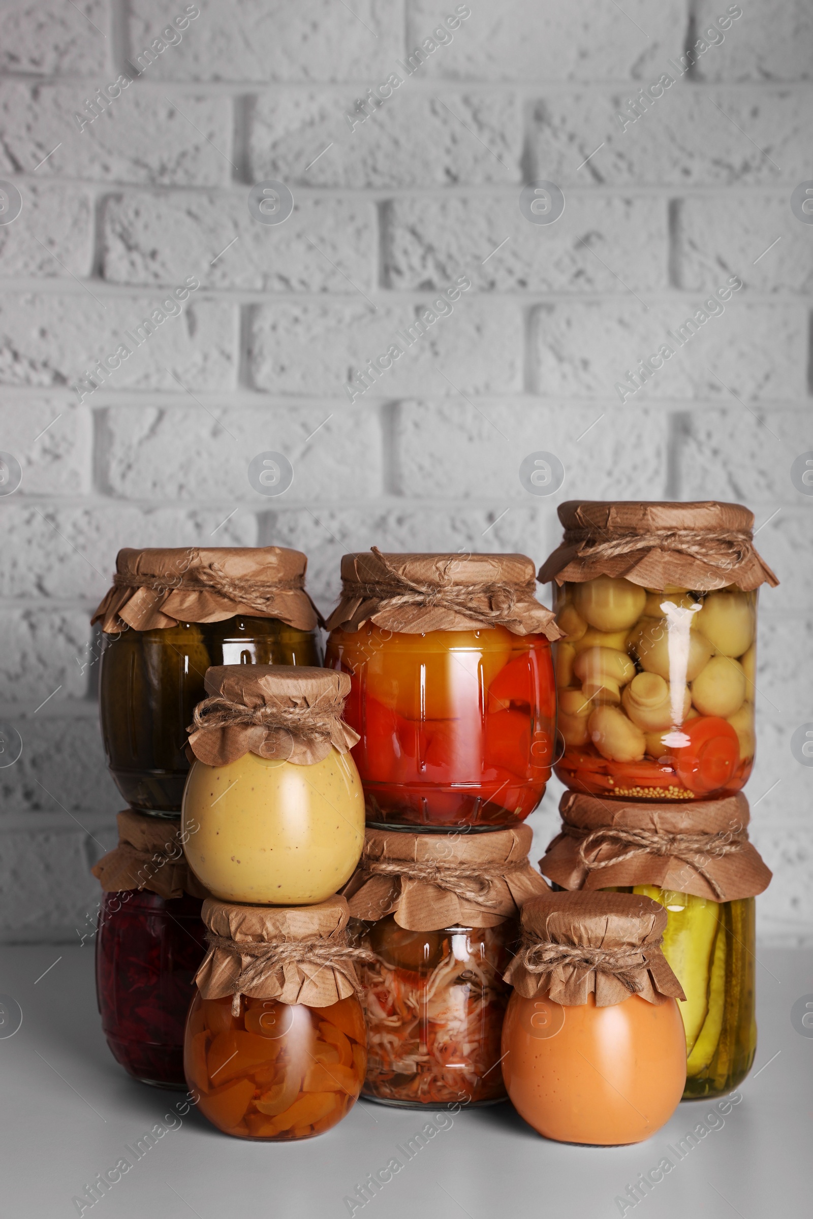 Photo of Many glass jars with different preserved products on light grey table