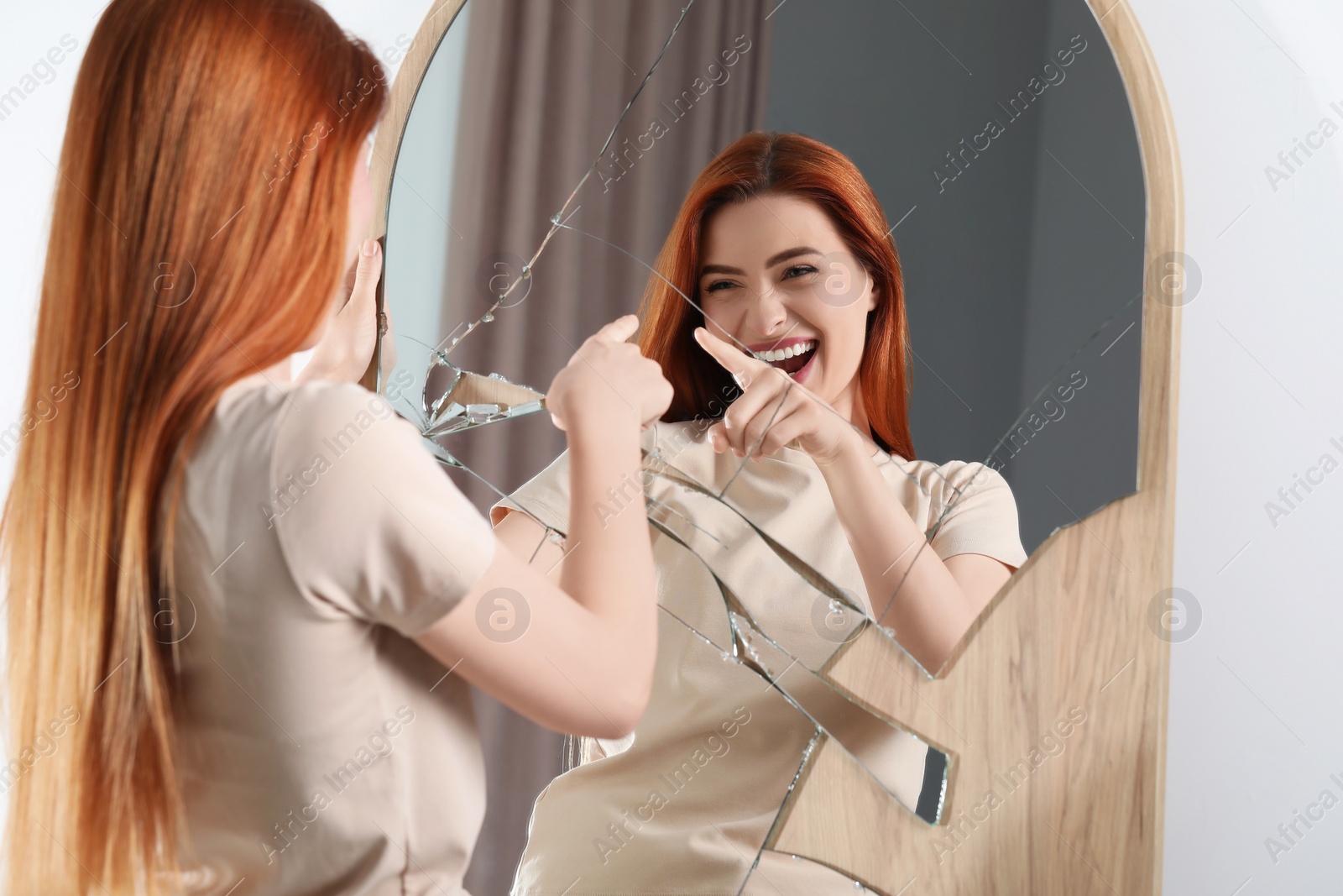 Photo of Mental problems. Young woman laughing near broken mirror indoors