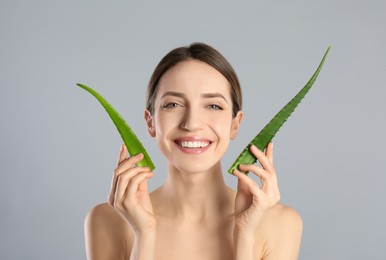 Photo of Happy young woman with aloe leaves on light grey background