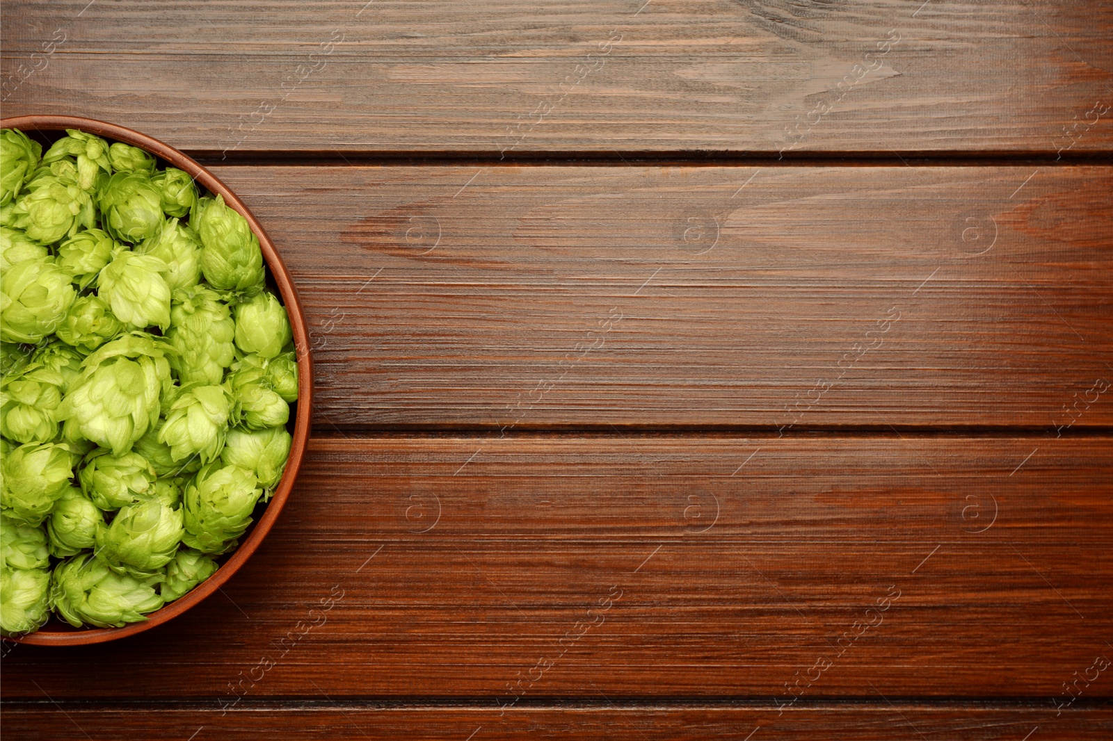 Photo of Bowl with fresh green hops on wooden table, top view. Space for text