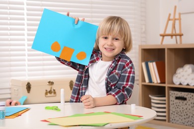 Cute little boy with colorful card at desk in room. Home workplace