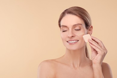 Photo of Woman blending foundation on face with makeup sponge against beige background. Space for text