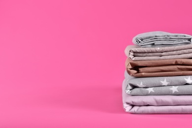 Photo of Stack of clean bed sheets on pink background. Space for text