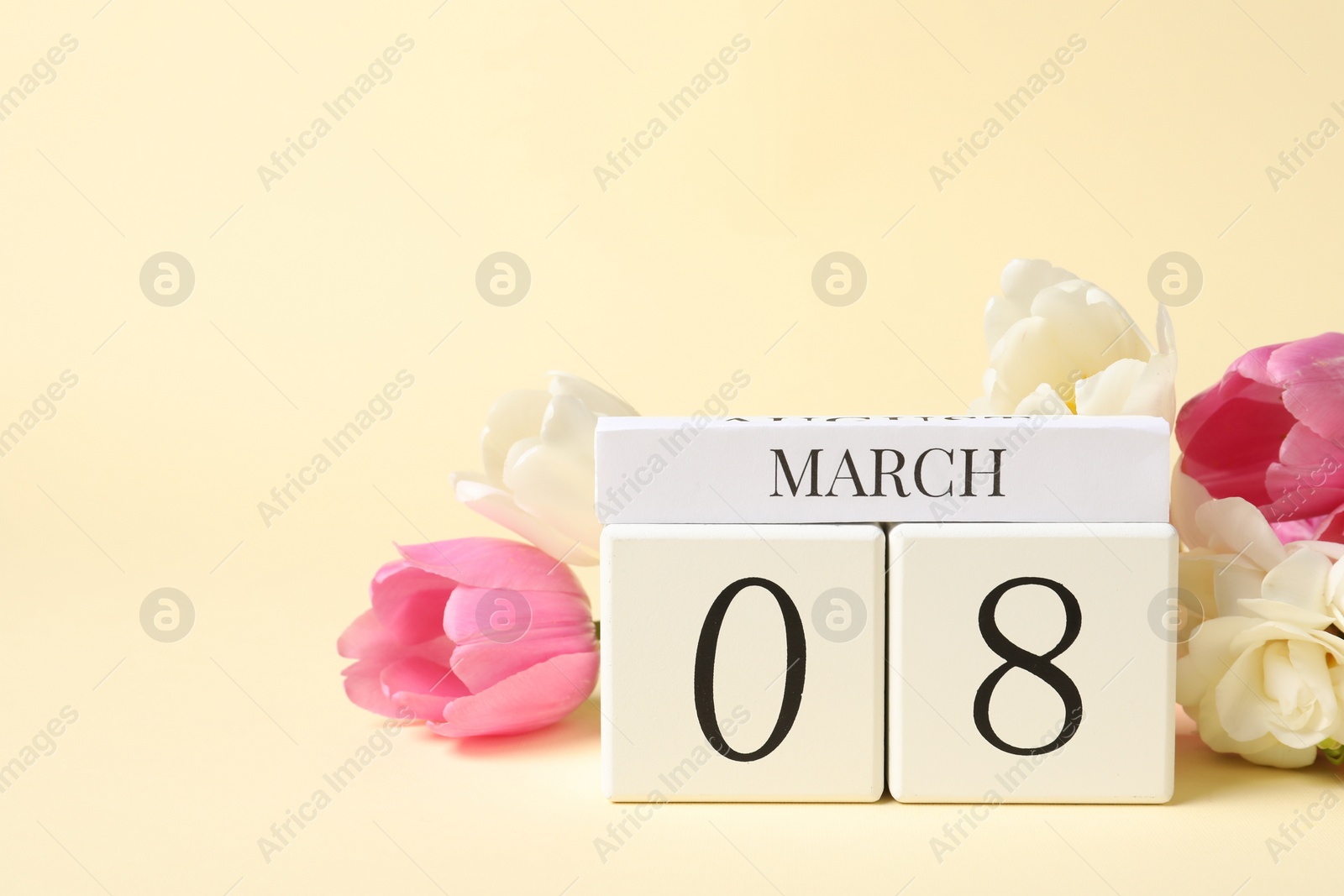 Photo of International Women's day - 8th of March. Wooden block calendar and beautiful flowers on beige background, space for text