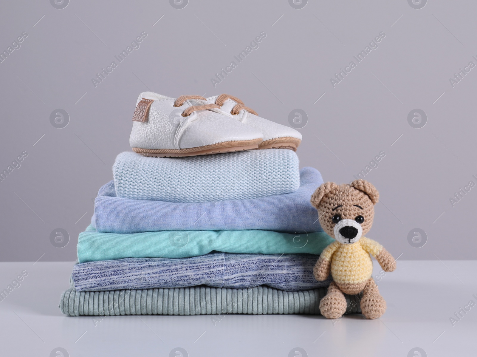 Photo of Stack of clean baby's clothes, toy and small shoes on table against light grey background. Space for text